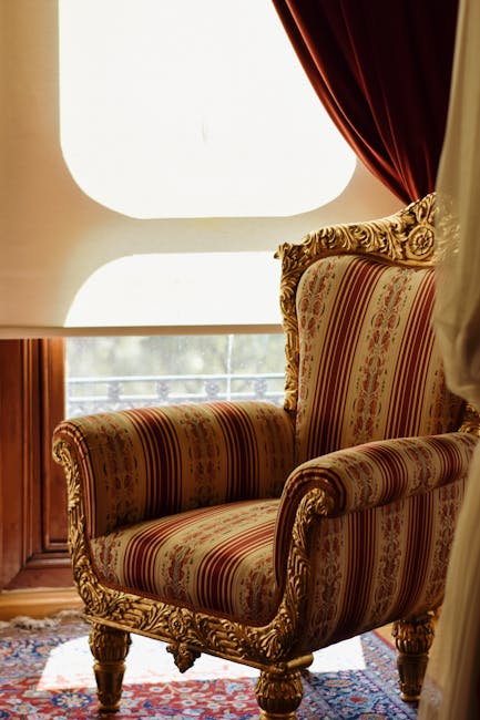 A close-up of a person's hand holding a handheld upholstery cleaning machine, which is being used to deep clean a beige fabric sofa seat. The machine's nozzle is pressed against the fabric, releasing