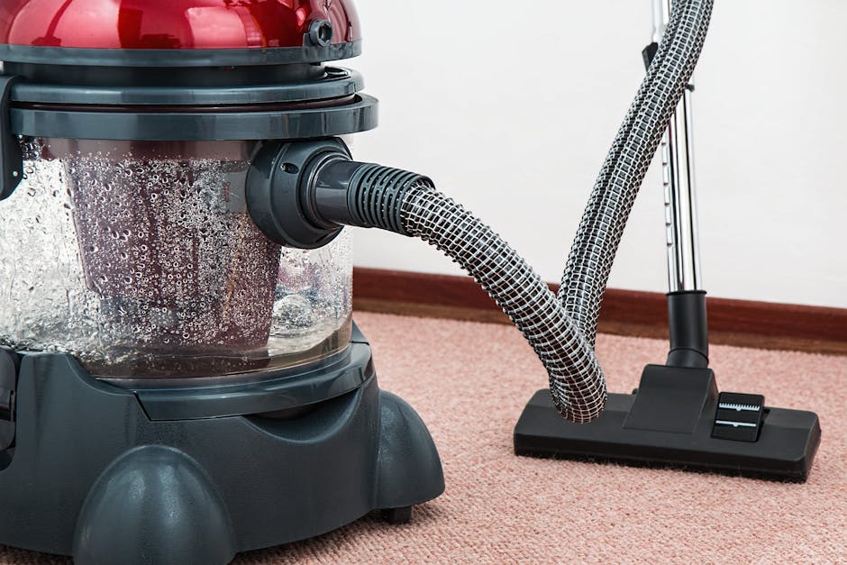 A person kneeling on a patterned carpet in a domestic setting, using a yellow and black vacuum cleaner for surface cleaning. The individual is focused on the vacuum’s attachments, with their hands a